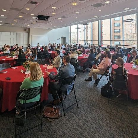 image of the full room of faculty, students and staff sitting at tables while the dean speaks to them from the front of the room 