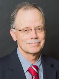 image of Emeritus Professor Ralph Taylor wearing glasses in a blue short, red tie and black suit jacket