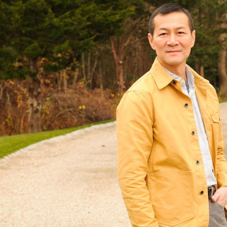 image of Don Lee standing in a yellow jacket, white shirt and grey pants with the woods in the background