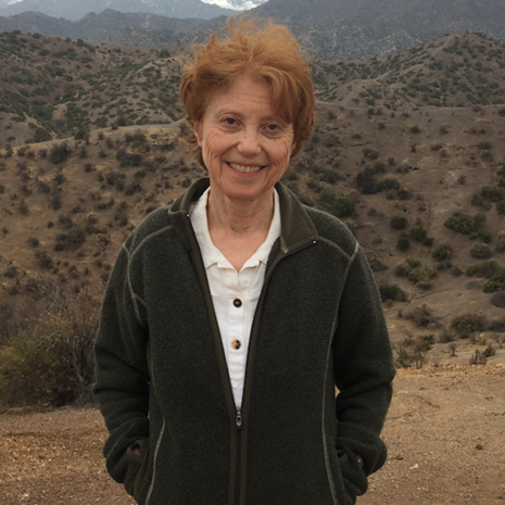 image of Nora standing in the desert wearing a black jacket smiling with the mountains behind her