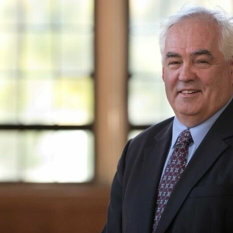 image of Peter wearing a black suit, sitting and smiling at the camera in Mitten Hall