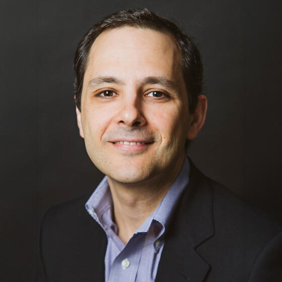 Pedro Silos wearing a black a suit coat with a blue shirt staring into the camera