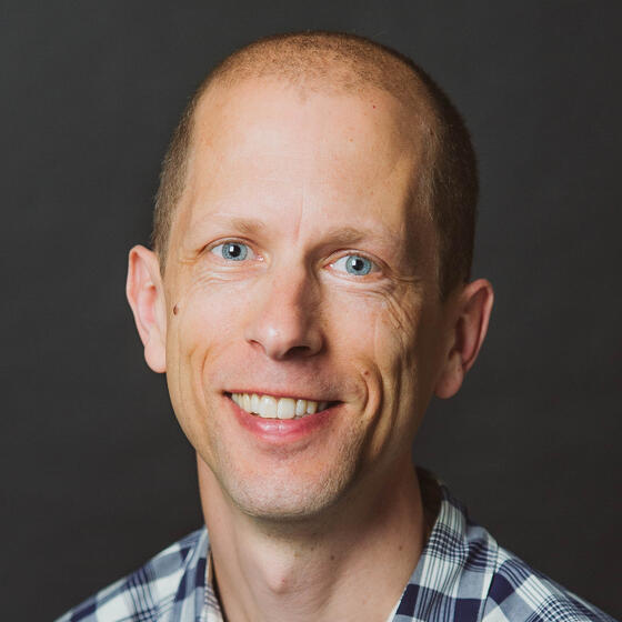 Peter J. Marshall in a black and white checkered shirt smiling and staring into the camera