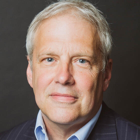 Robert Fauber in a black suit with a blue shirt staring into the camera