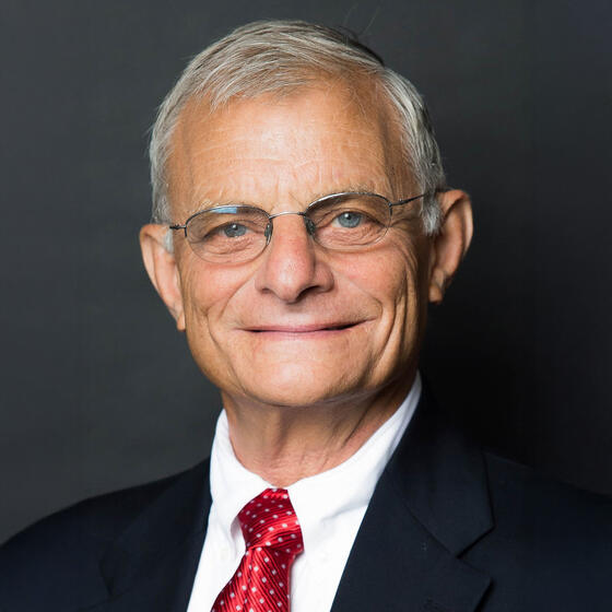 Simon Hakim wearing a black suit with a red tie smiling and staring into the camera