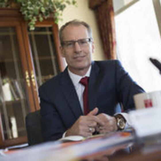 Richard Deeg in his office wearing a navy suit with a red tie smiling and staring into the camera
