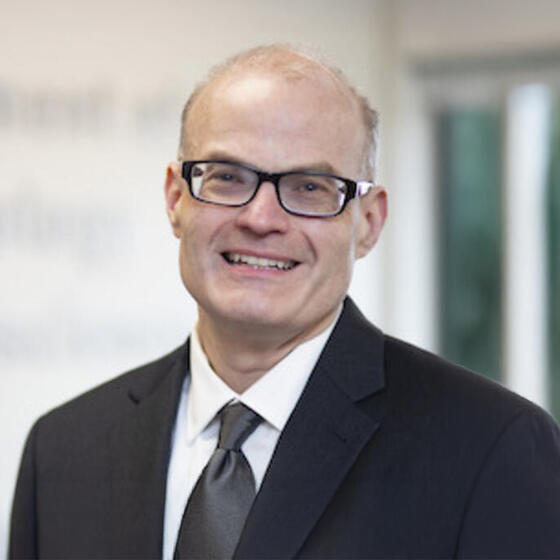 Joshua Klugman in a black suit and tie smiling and staring into the camera