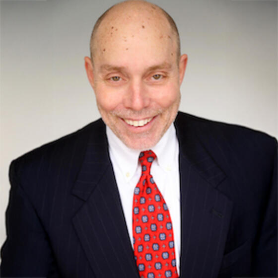 Christopher Swann wearing a black suit and red tie smiling and staring into the camera