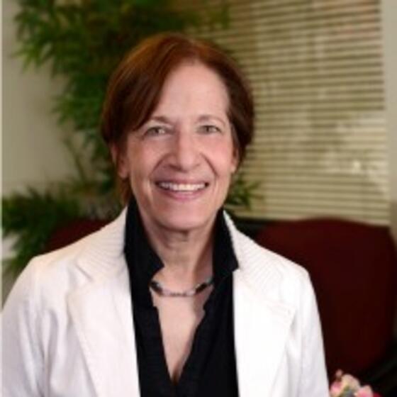 Kathryn Hirsh-Pasek in white suit coat with a black shirt smiling and staring into the camera