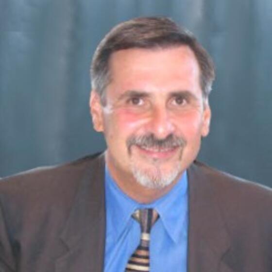 Gary Mucciaroni in a gray suit with a blue shirt on smiling and staring into the camera