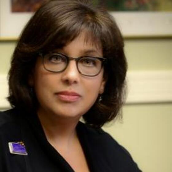 image of Pam wearing glasses wearing a suit looking at the camera