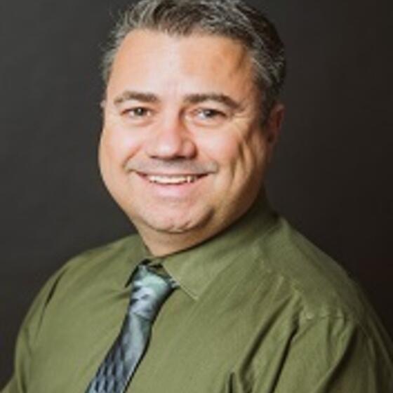 Peter James in a green shirt with a gray tie smiling and staring into the camera