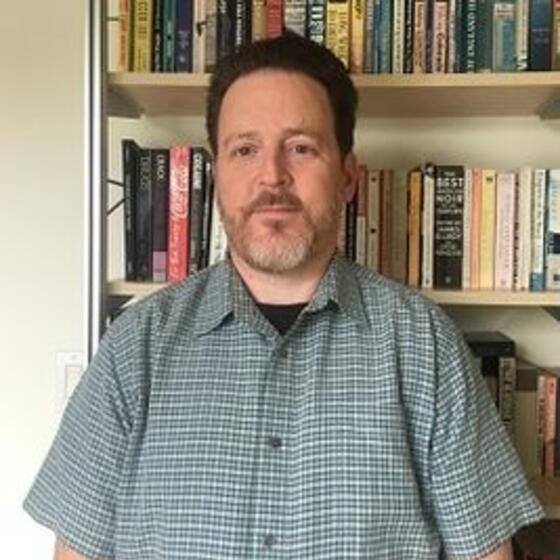 Hillel David Soifer in front of a book shelf staring into the camera