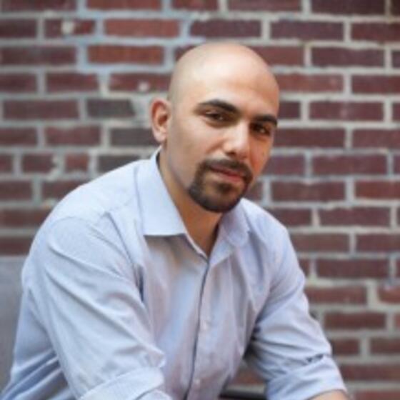 Mathieu Wimmer in a light blue shirt sitting in front of a brick wall staring into the camera