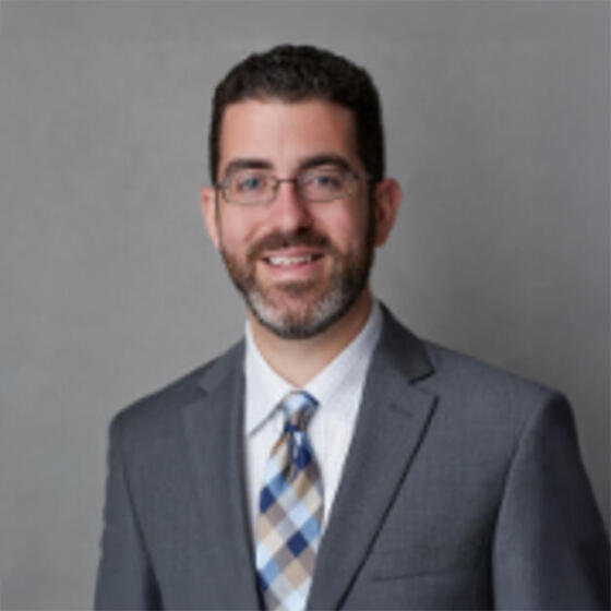 Michael Sances in a gray suit and tie smiling and staring into the camera