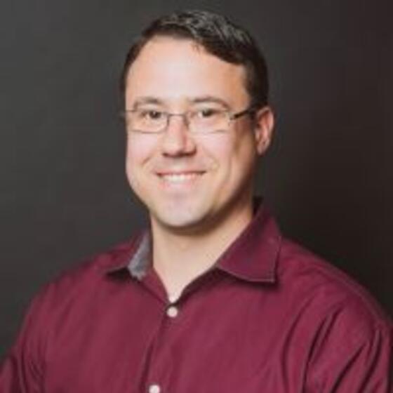 Timothy Garelick in a red shirt smiling and staring into the camera
