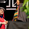 image of Dean Richard Deeg in graduation regalia shaking a students name on the graduation stage