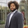 headshot of Nyron standing in a suit on Mazur terrace smiling at the camera