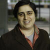 headshot of Wazhmah wearing a brown jacket and red shirt and smiling at the camera
