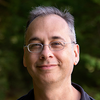 image of Mark standing outside wearing glasses and smiling at the camera