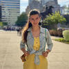 Angela Mejia in a yellow jump suit and jean jacker standing outside staring into the camera