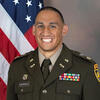 Anthony Guerrero in an Army uniform in front of an American flag smiling into the camera