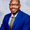 Bako Bapio Pierre in a blue suit with a blue and gold tie smiling into the camera