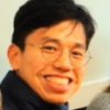 image of Han wearing glasses and a black turtleneck smiling at the camera