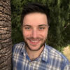 Matthew Marcus in blue and white shirt standing next to a tree smiling into the camera