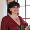 Kelly Haggerty in a red dress holding flowers in front of a window smiling into the camera