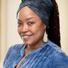 image of Vangie wearing a blue denim top with her hair wrapped up smiling at the camera