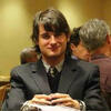Casey VanSise sitting at a table in a gray suit and tie staring into the camera