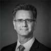 black and white image of Alan wearing a suit and glasses smiling at the camera
