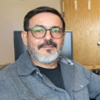 Esteban Lopez-Arguedas in a gray shirt sitting at a desk staring into the camera