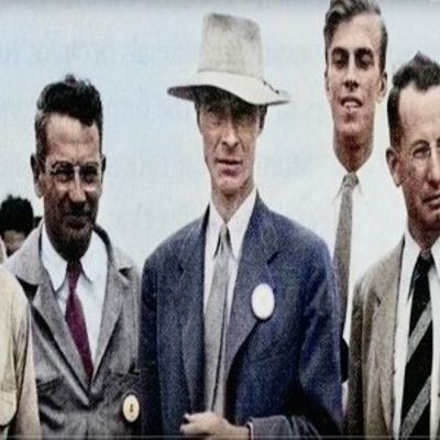 image of Oppenheimer wearing a tan hat and suit standing with other men in suits 