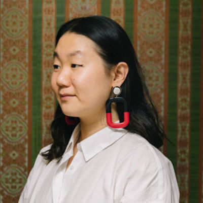 image of Wendy standing in a profile view wearing a white blouse and red earrings