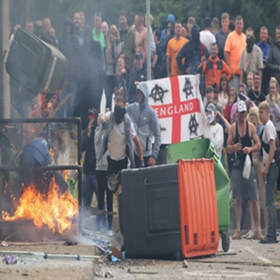 image of protesters in England standing in a group setting a trash can on fire