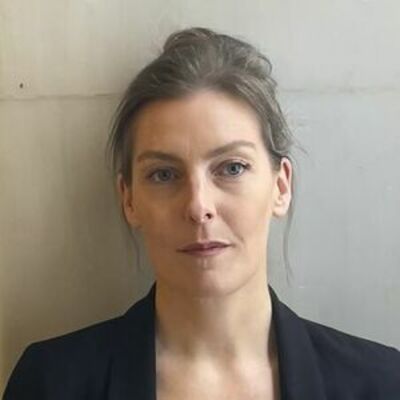 image of Caolinn with a high bun looking at the camera, not smiling, wearing a black suit jacket