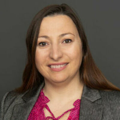 headshot of Silvia smiling at the camera, wearing a grey blazer and red top