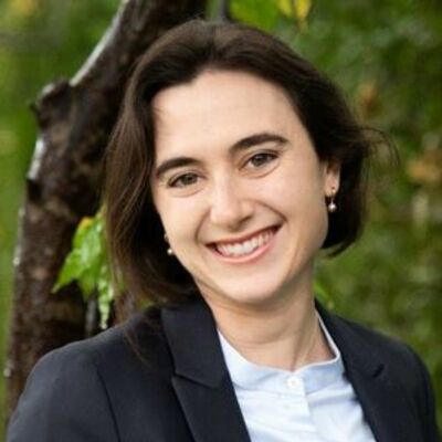image of Kathering wearing a black suit jacket, smiling at the camera with a tree in the background