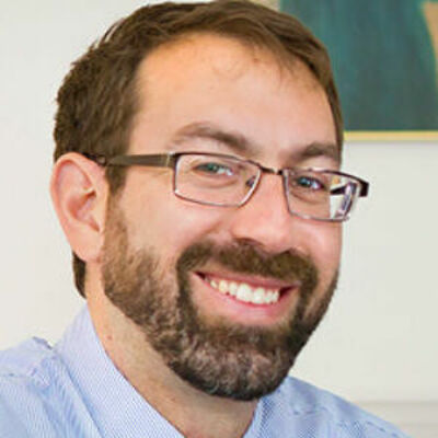 image of Samuel wearing a blue dress shirt and glasses, amiling at the camera