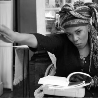 image of Julie in black and whitewearing a head scarf and black top looking at the camera and pointing with her right hand