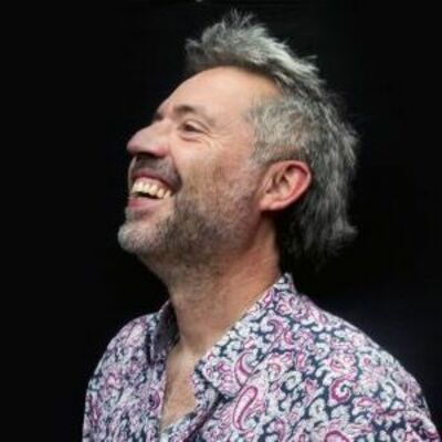 image of Oscar wearing a floral shirt against a black background looking off into the distance and smiling
