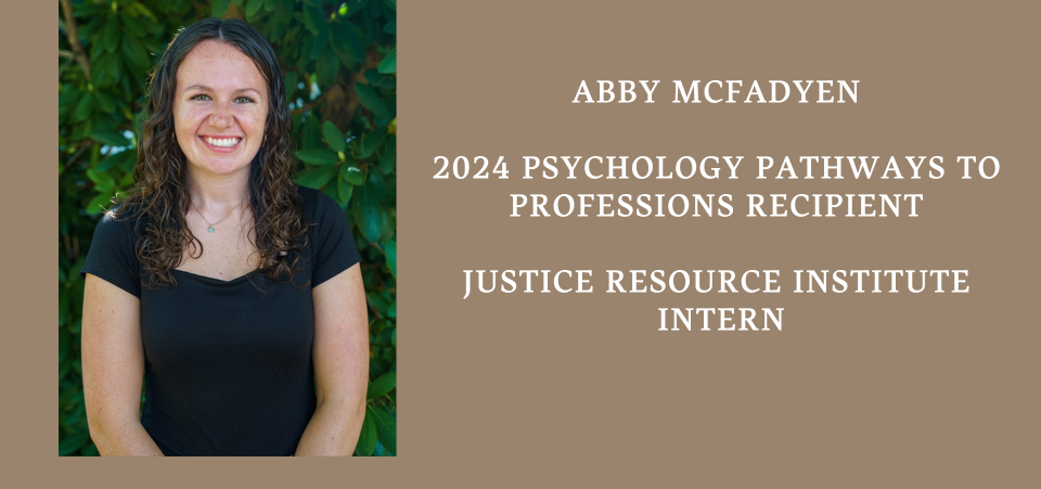 image of Abby smiling at the camera wearing a black blouse standing in front of green trees