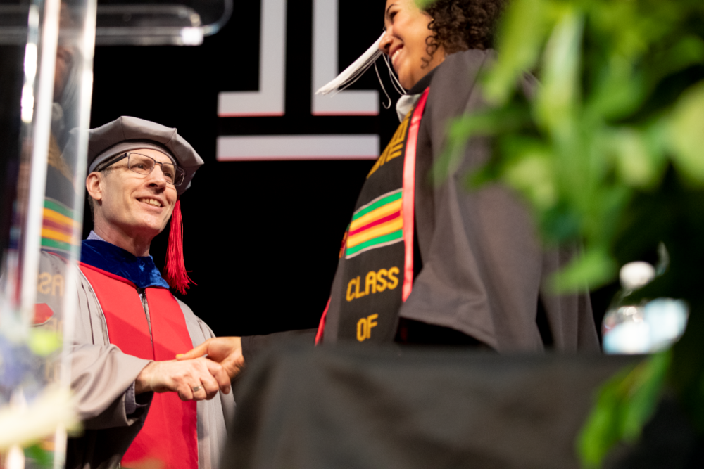image of Dean Richard Deeg in graduation regalia shaking a students name on the graduation stage