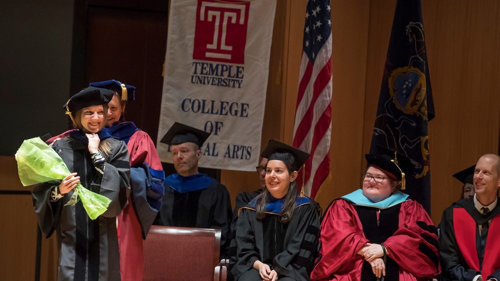 doctoral student receiving her regalia stage while professors watch