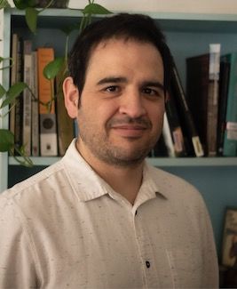 image of Jeronimo Rodriquez standing in front of a teal bookcase with a white dress shirt on
