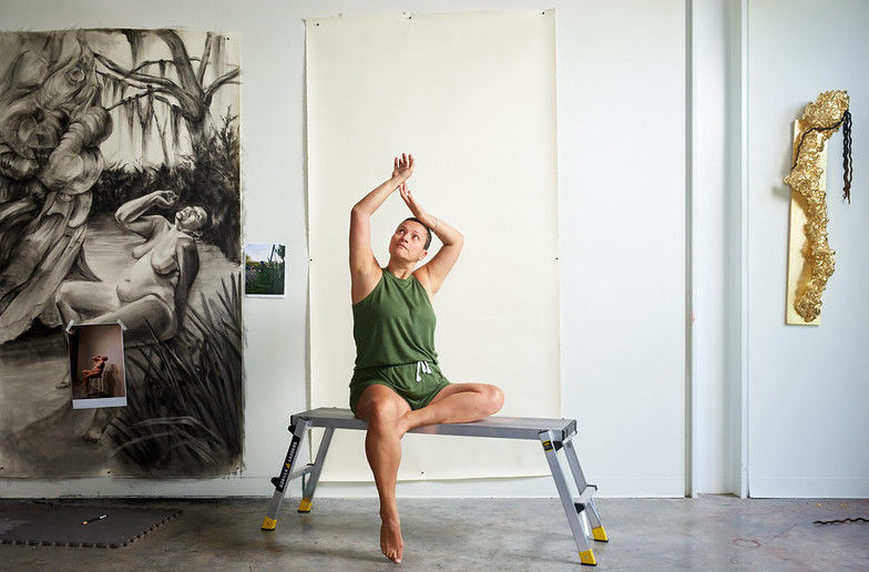 image of Wanda sitting on a bench weaing green shorts and top holding her arms above her head posed