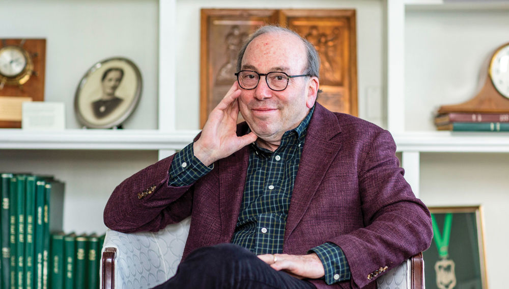 image of Witney sitting with his hand on his chin in a maroon blazer and blue dress shirt