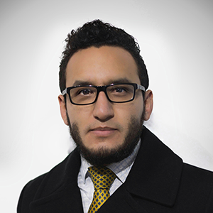 image of Alex wearing glasses with a black suit jacket, white shirt and gold tie